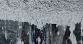 Detailansicht einer hellen, feuchten Betonoberfläche. Der Beton läuft an einer Kante herab, sodass die Struktur und die flüssige Konsistenz deutlich sichtbar werden. Die Oberfläche wirkt frisch gegossen und noch nicht ausgehärtet